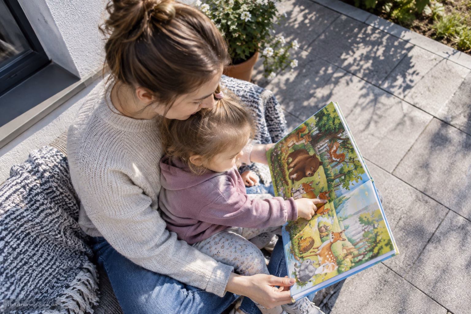 Мама тримає книжку з картинками, а малюк показує на ілюстрацію тварини